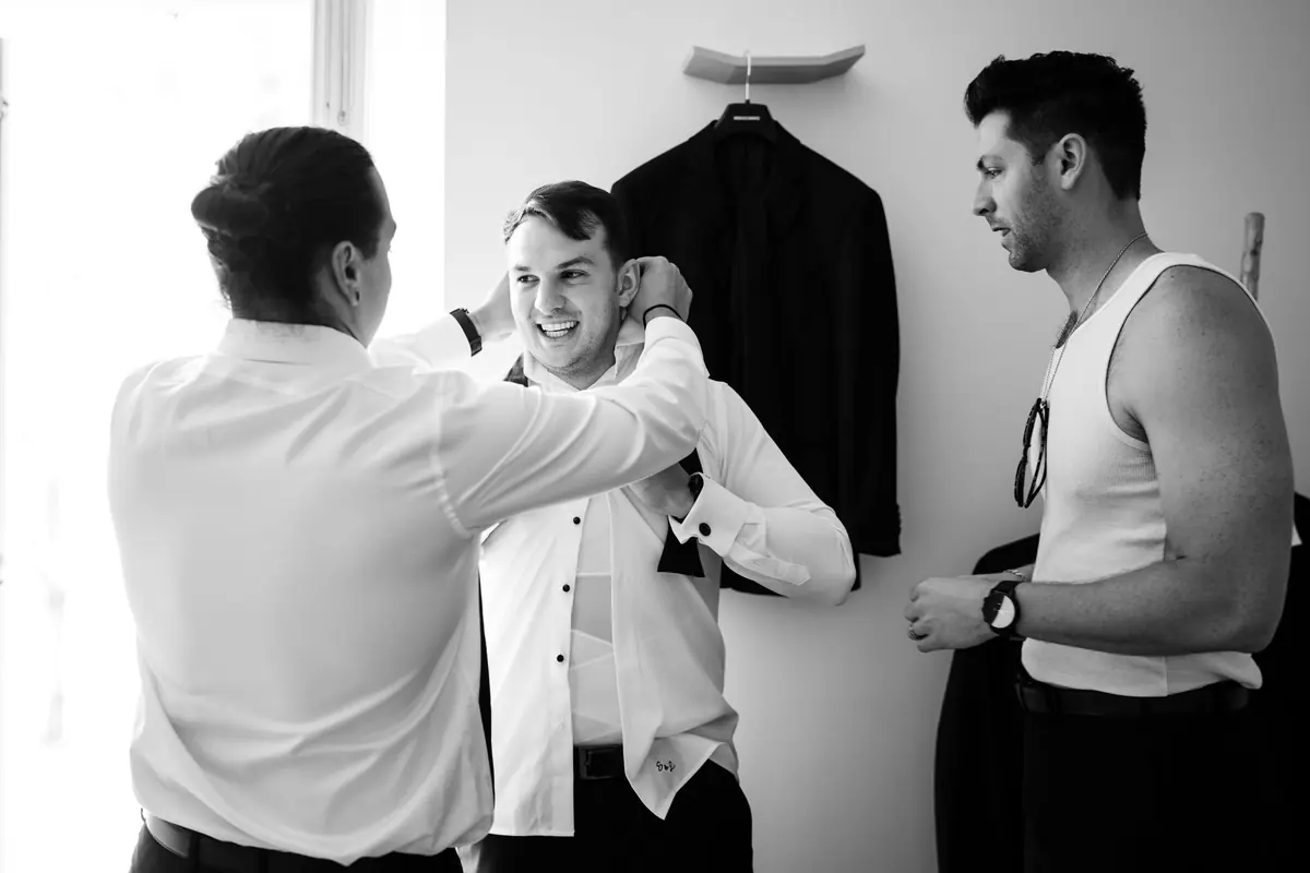 Drew's groomsmen helping him into his shirt, in black and white
