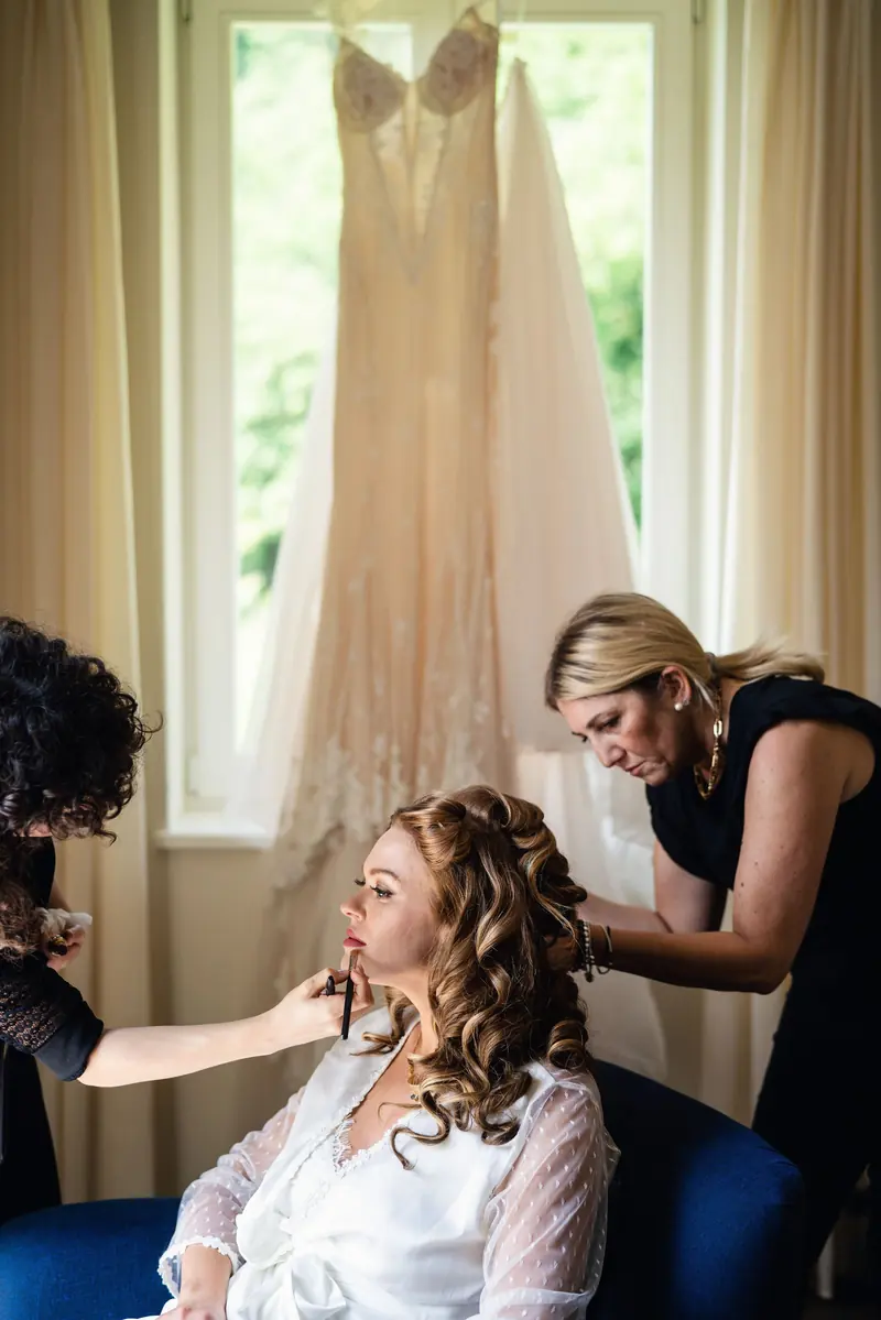 Bride having her make-up done by the window, with her gown hanging behind