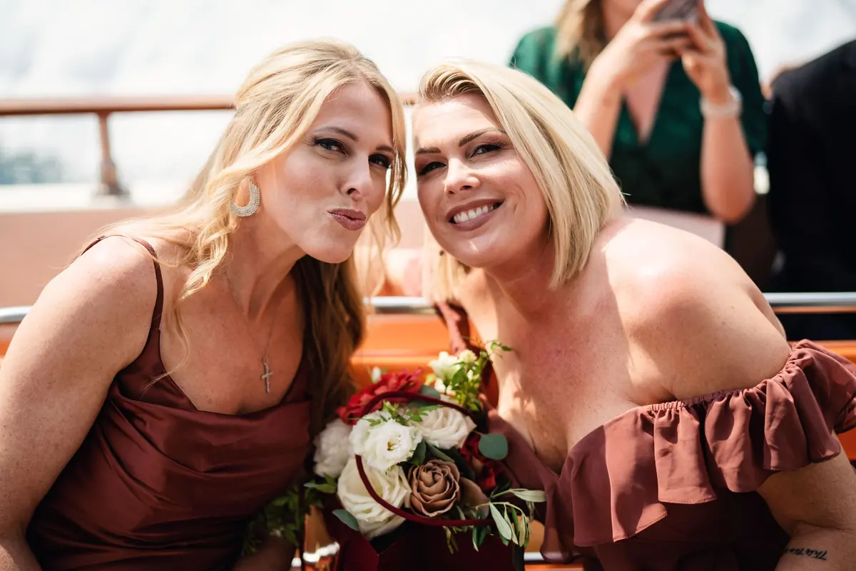 Two bridesmaids in rose dresses laughing on the boat