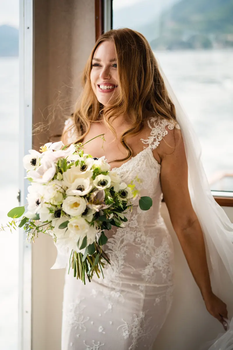 Sara with her bouquet by the boat window, the lake behind her