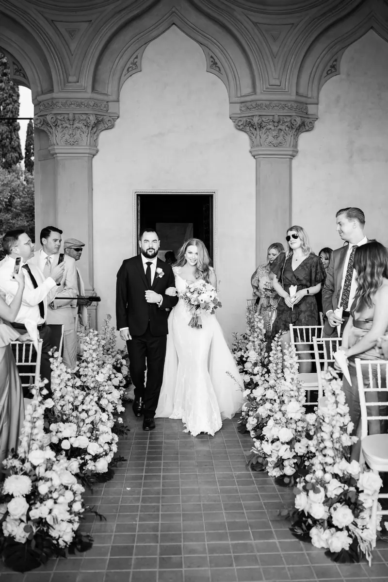 Black and white photo of the bride walking down the flower-lined aisle