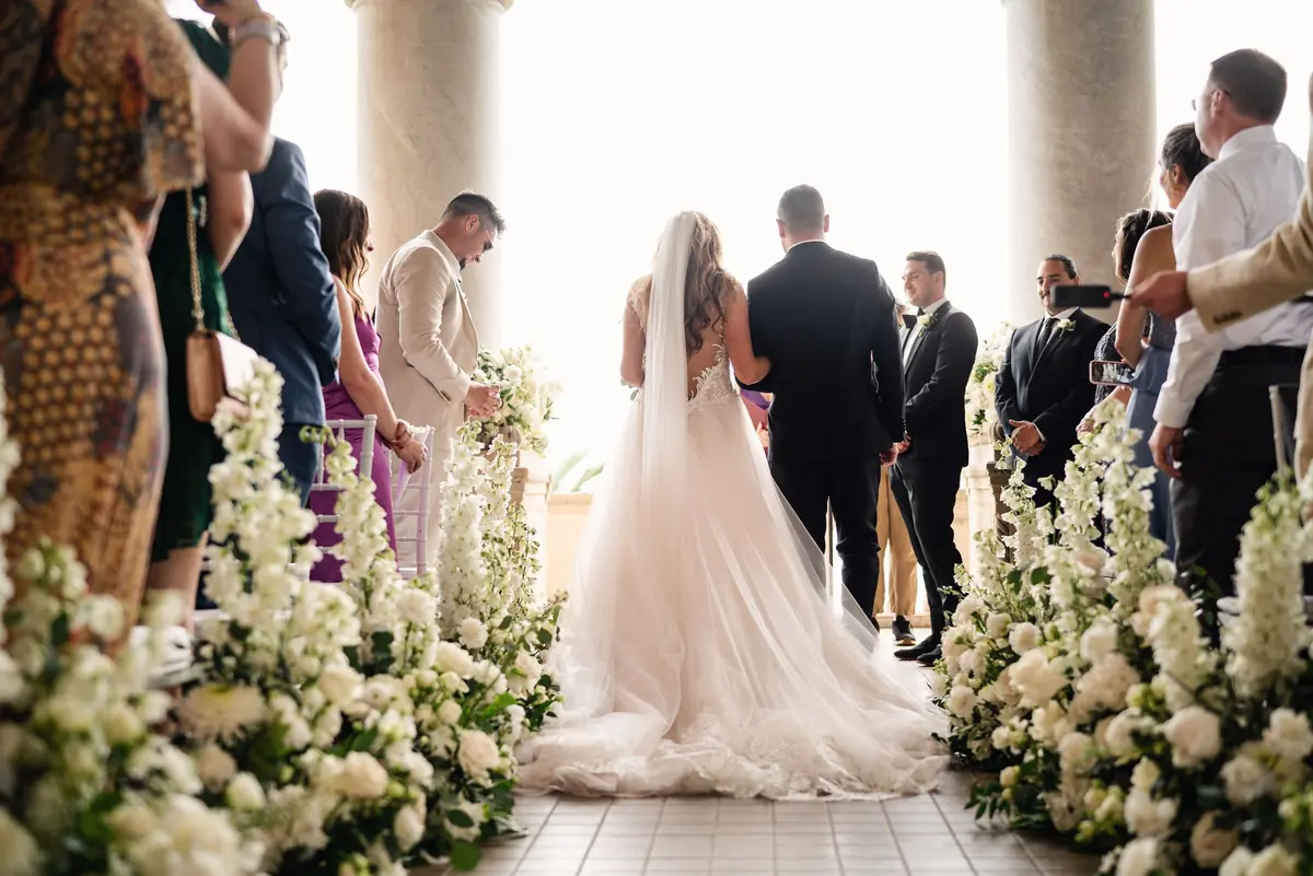 Sara walking down the flower-lined aisle towards Drew