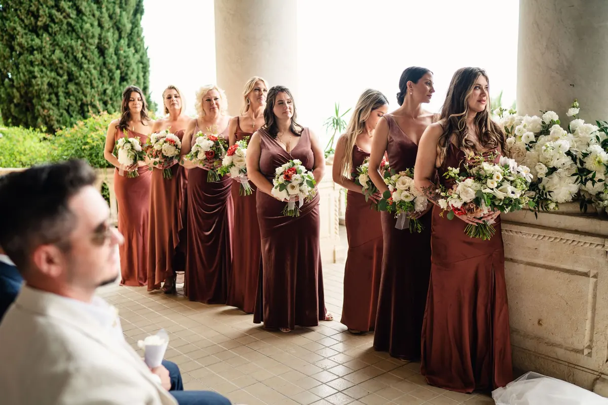 The bridesmaids in rust satin standing along the loggia