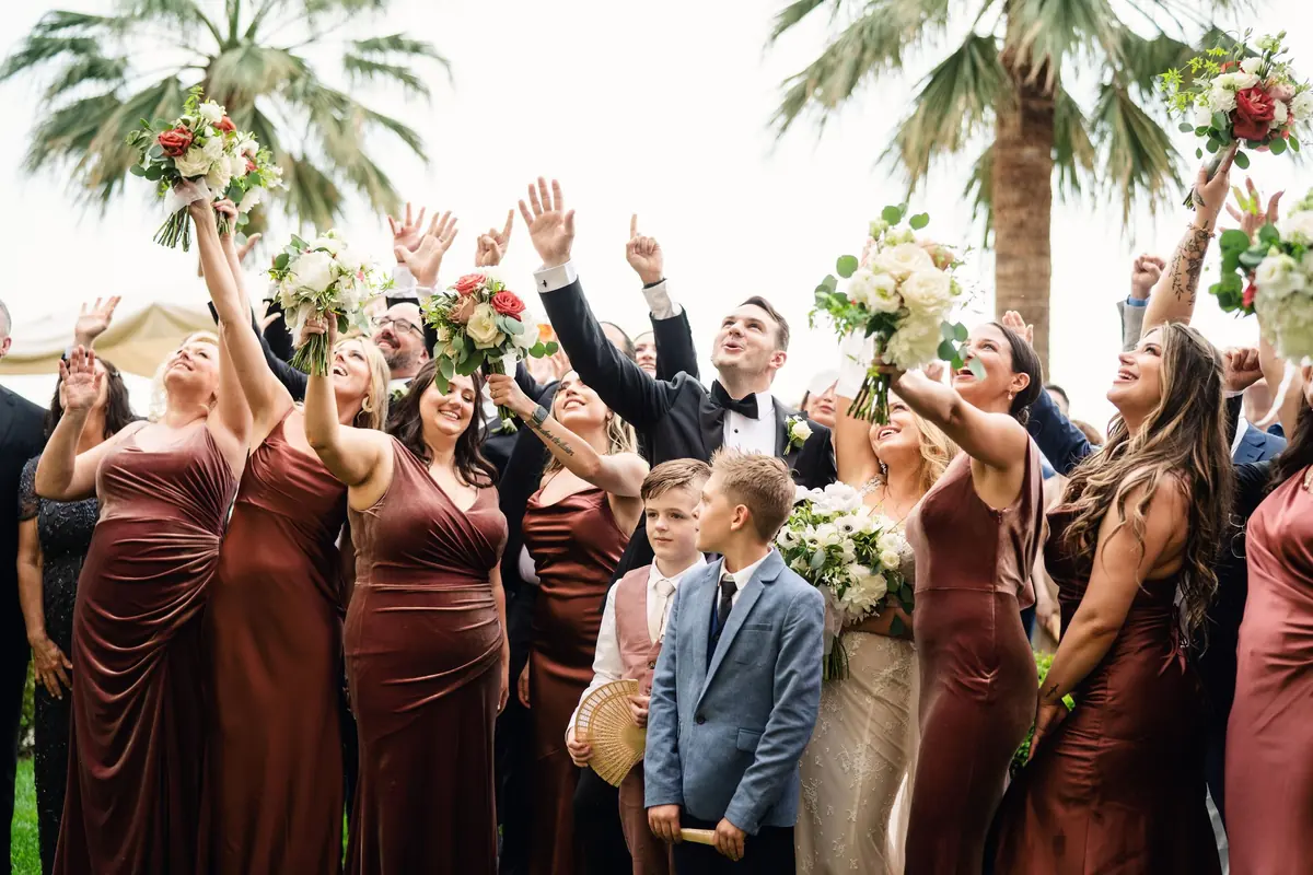 The bridesmaids cheering with their bouquets under the palm trees