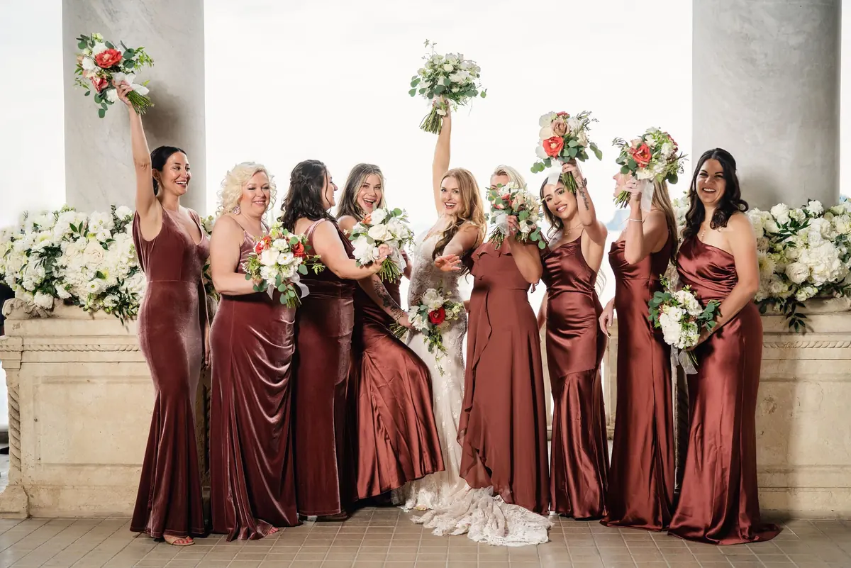 The bridesmaids raising their bouquets around Sara