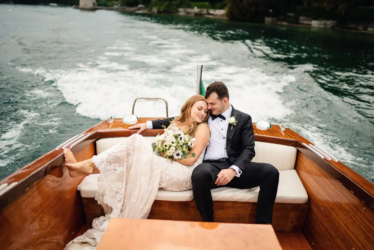 Newlyweds at the stern of the Riva boat with its wake behind
