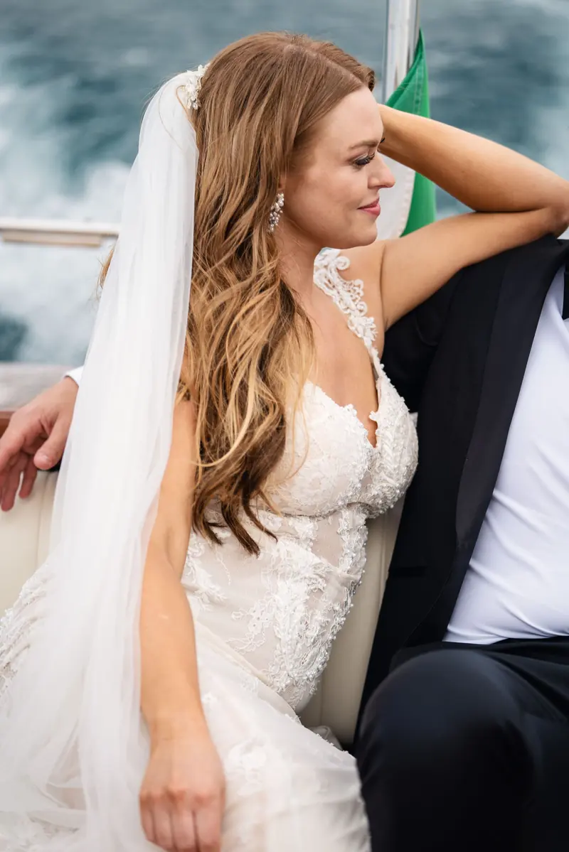 Sara leaning back in the Riva boat, her veil in the breeze