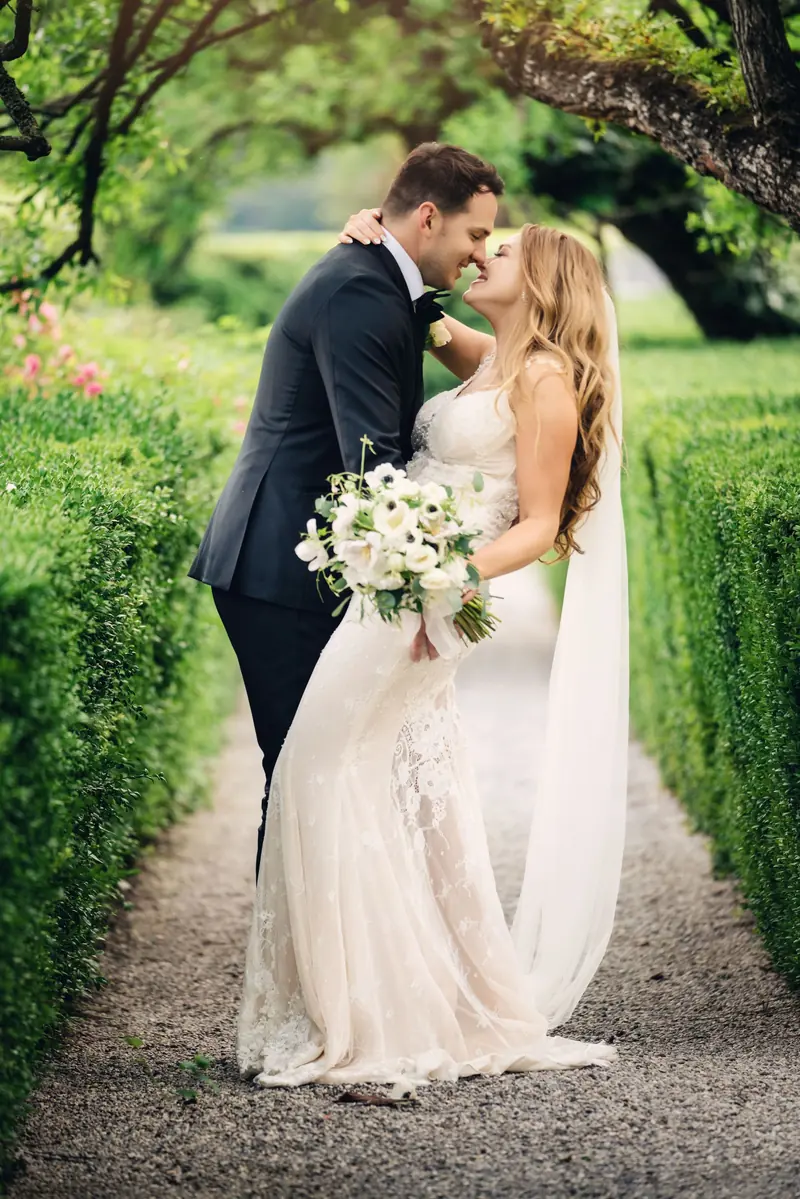 Sara and Drew embracing on a hedge-lined garden path
