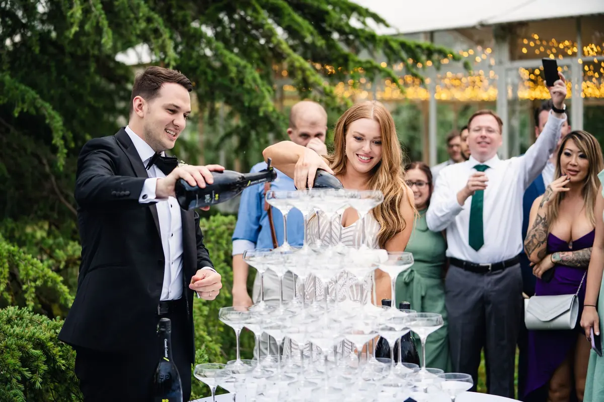 Drew pouring the champagne tower as Sara and guests watch