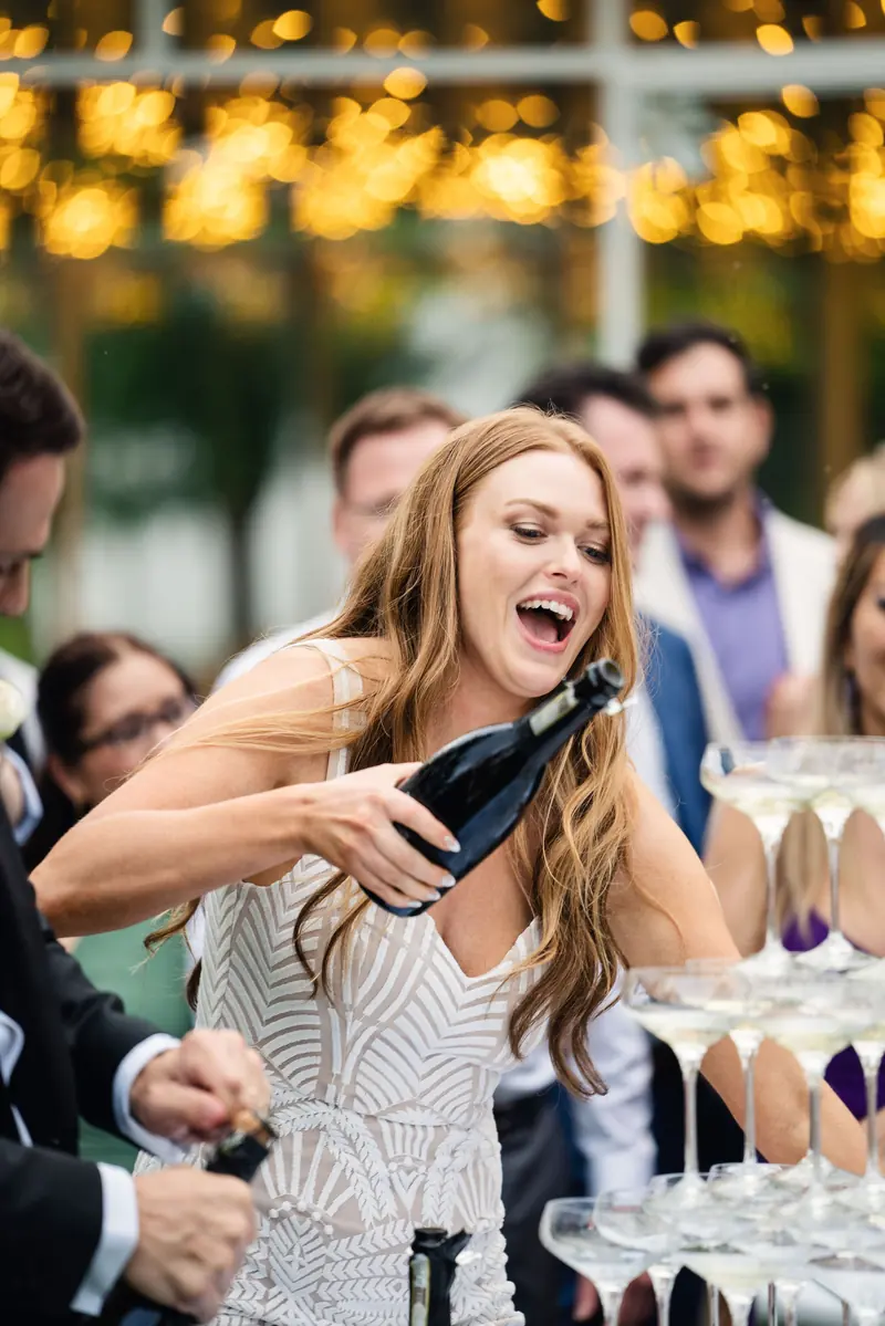 Bride laughing as she pours champagne at the champagne tower