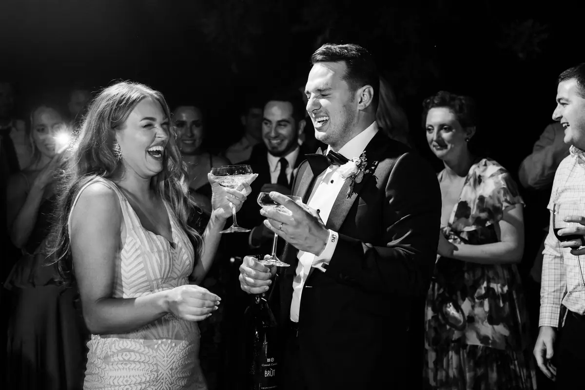 Sara and Drew laughing with drinks at the party, in black and white